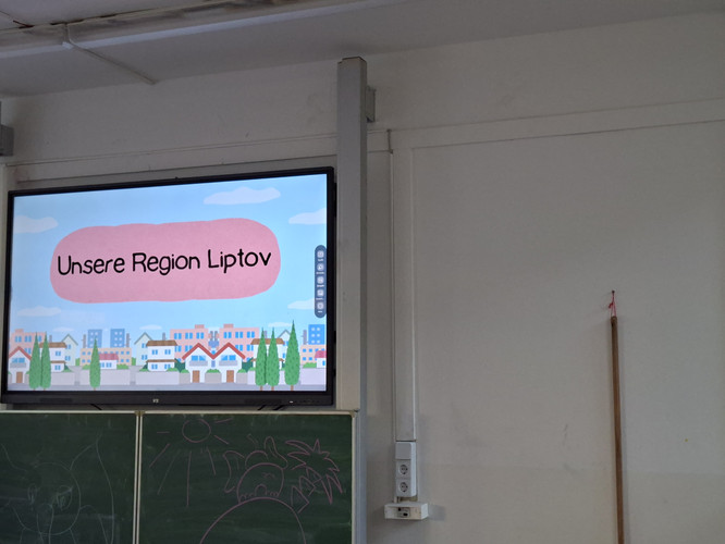 KI generiert: Das Bild zeigt ein Klassenzimmer mit einem Bildschirm, auf dem "Unsere Region Liptov" steht, sowie eine Tafel mit Zeichnungen. Der Hauptinhalt ist eine Präsentation über die Region Liptov.