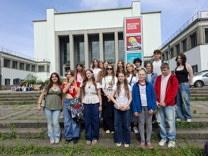 KI generiert: Eine Gruppe von jungen Menschen steht vor dem Deutschen Hygiene-Museum auf einer Treppe. Im Hintergrund ist das Museumsgebäude zu sehen.