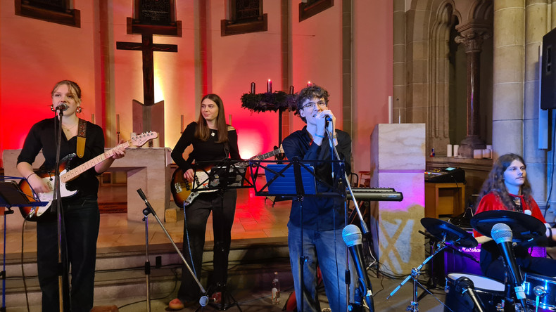 KI generiert: Das Bild zeigt eine Musikgruppe, die in einem kirchlichen Ambiente mit farbiger Beleuchtung auftritt. Die Musiker spielen verschiedene Instrumente wie Gitarre und Schlagzeug.