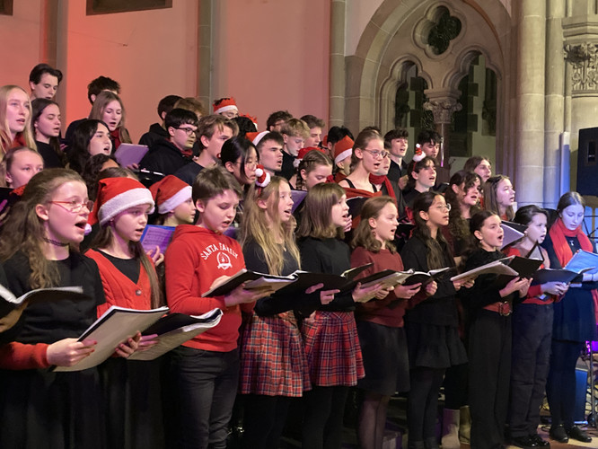 KI generiert: Das Bild zeigt eine Gruppe von singenden Jugendlichen, die ein Chorkonzert in einem festlich dekorierten Raum geben. Einige der Sänger tragen Weihnachtsmützen, was auf ein weihnachtliches Thema hindeutet.