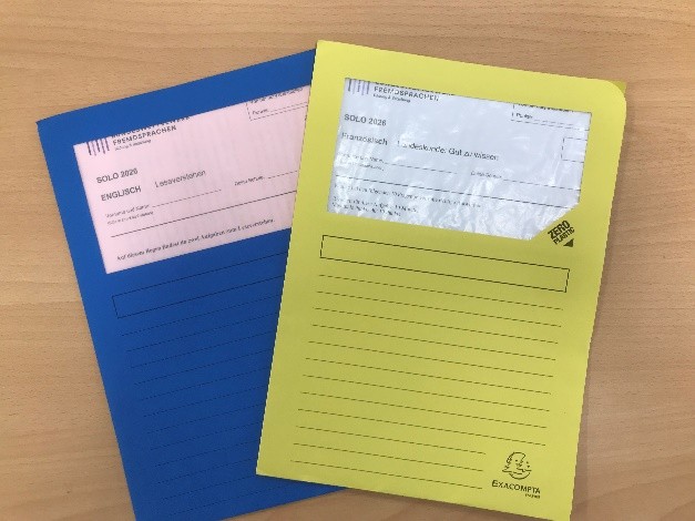 KI generiert: Das Bild zeigt zwei farbige Heftumschläge, einen blauen und einen gelben, mit Aufschriften für Schulunterlagen in den Fächern Englisch und Französisch auf einem Tisch. Die Umschläge tragen Labels mit Informationen zu den jeweiligen Sprachfächern.