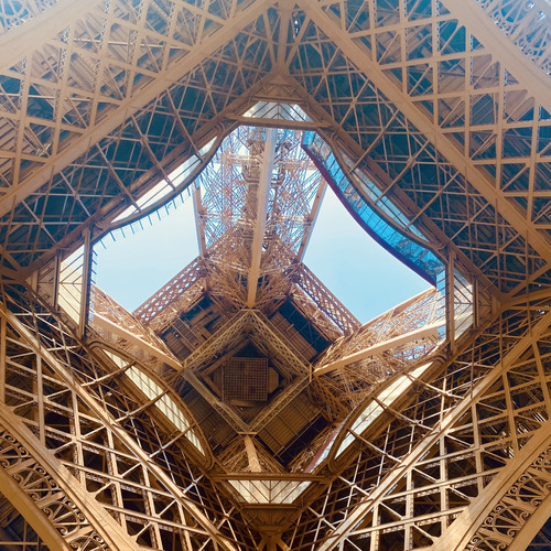 KI generiert: Das Bild zeigt die komplexe Stahlkonstruktion unter dem Eiffelturm, mit Blick nach oben in die Architektur. Der Hauptinhalt ist das detaillierte Gitterwerk des Turmes.