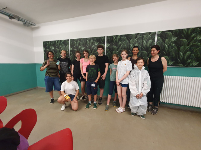 KI generiert: Das Bild zeigt eine Gruppe von Menschen in einem Raum, die entspannt posieren. Im Hintergrund sind Wandbilder mit Blattmotiven zu sehen.