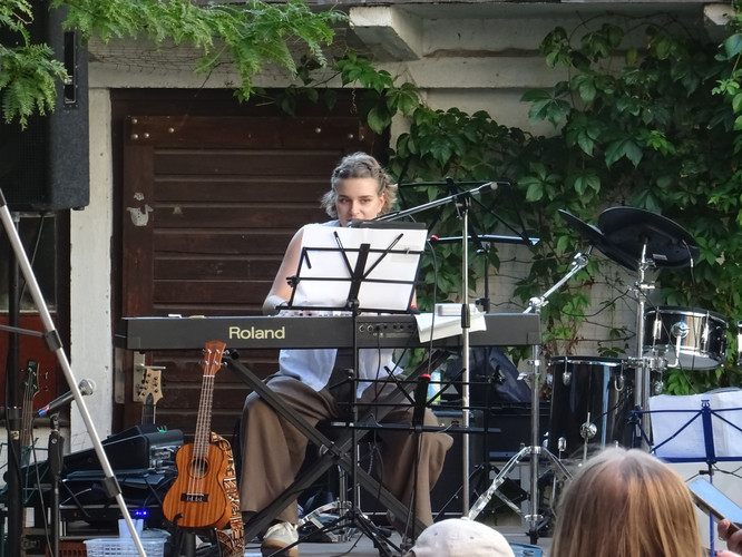 KI generiert: Eine Person spielt auf einer Bühne ein elektrisches Klavier. Im Hintergrund sind weitere Musikinstrumente wie ein Schlagzeug erkennbar.