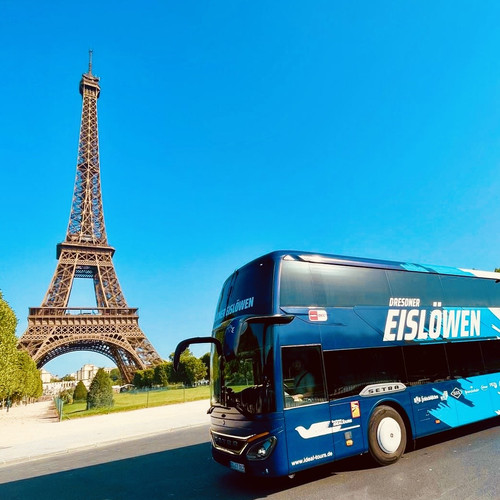 KI generiert: Das Bild zeigt einen blauen Reisebus mit der Aufschrift "Dresdner Eislöwen" vor dem Eiffelturm in Paris. Der Bus steht auf einer Straße mit dem berühmten Wahrzeichen im Hintergrund.